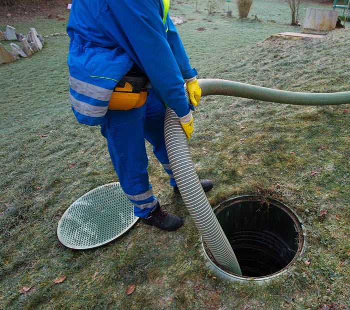 A man is pumping water into a septic tank with a hose.