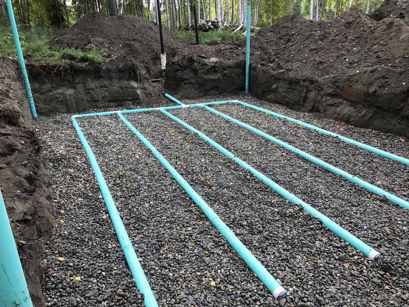 A row of green pipes are lined up in a pile of gravel.