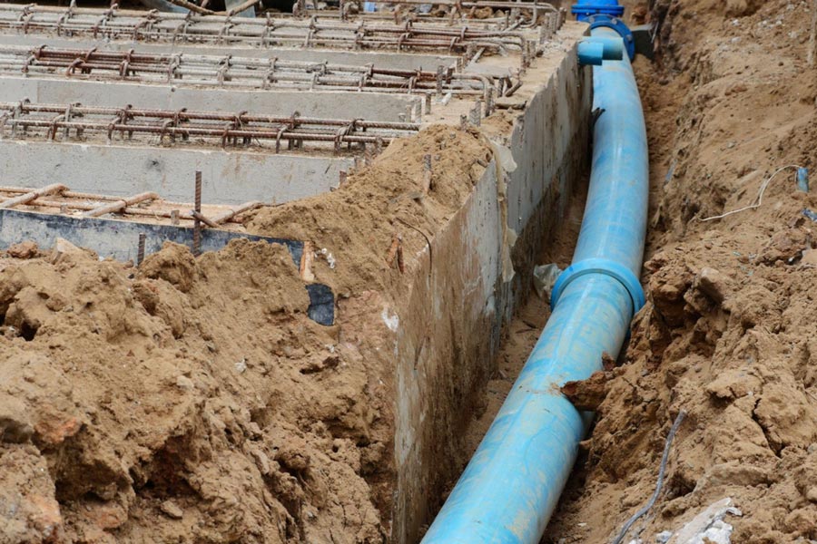 A blue pipe is being installed in the dirt at a construction site.