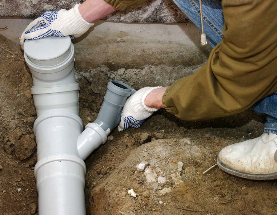 A man is working on a drain pipe in the dirt.