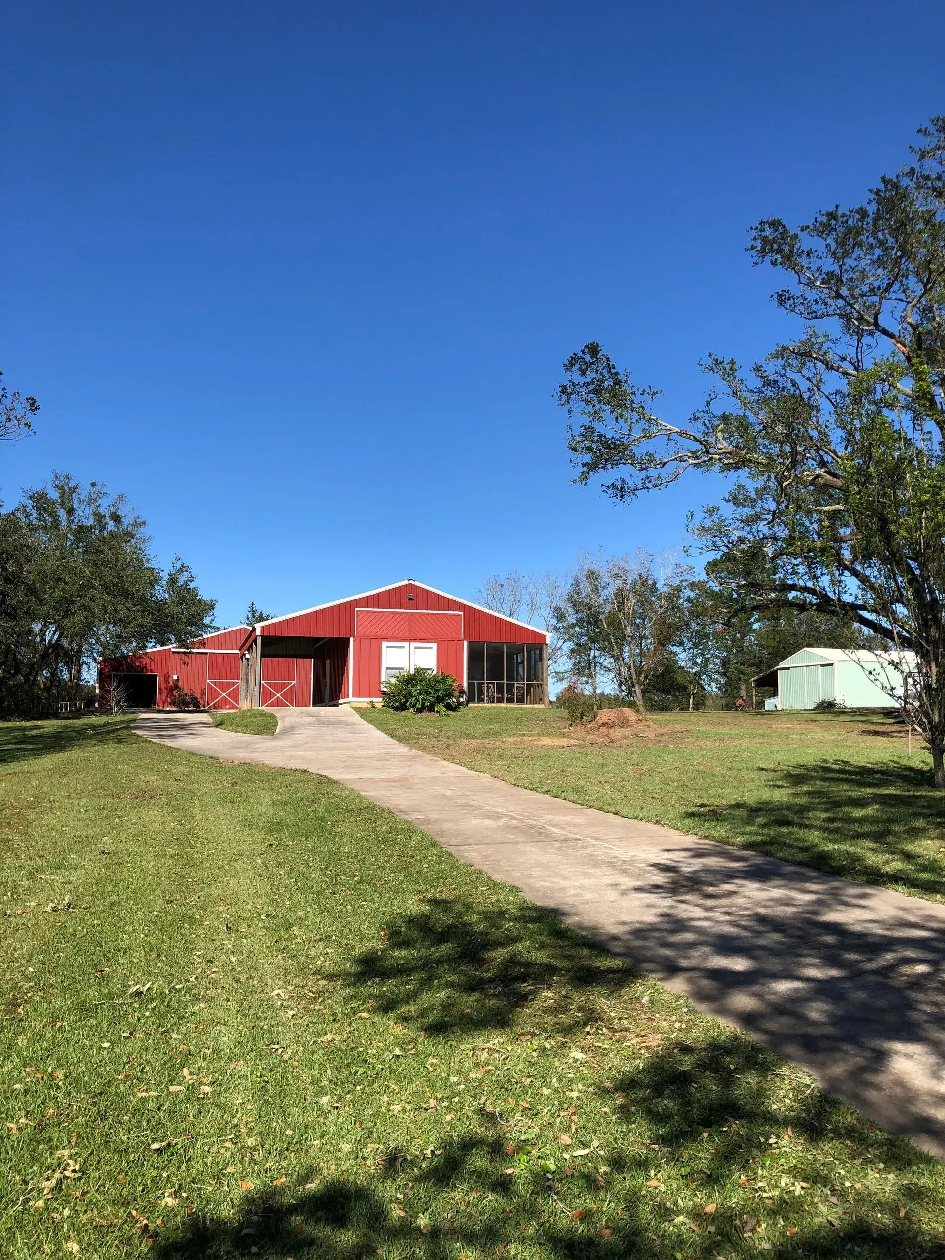 Red building with a driveway and green lawn under a bright blue sky.