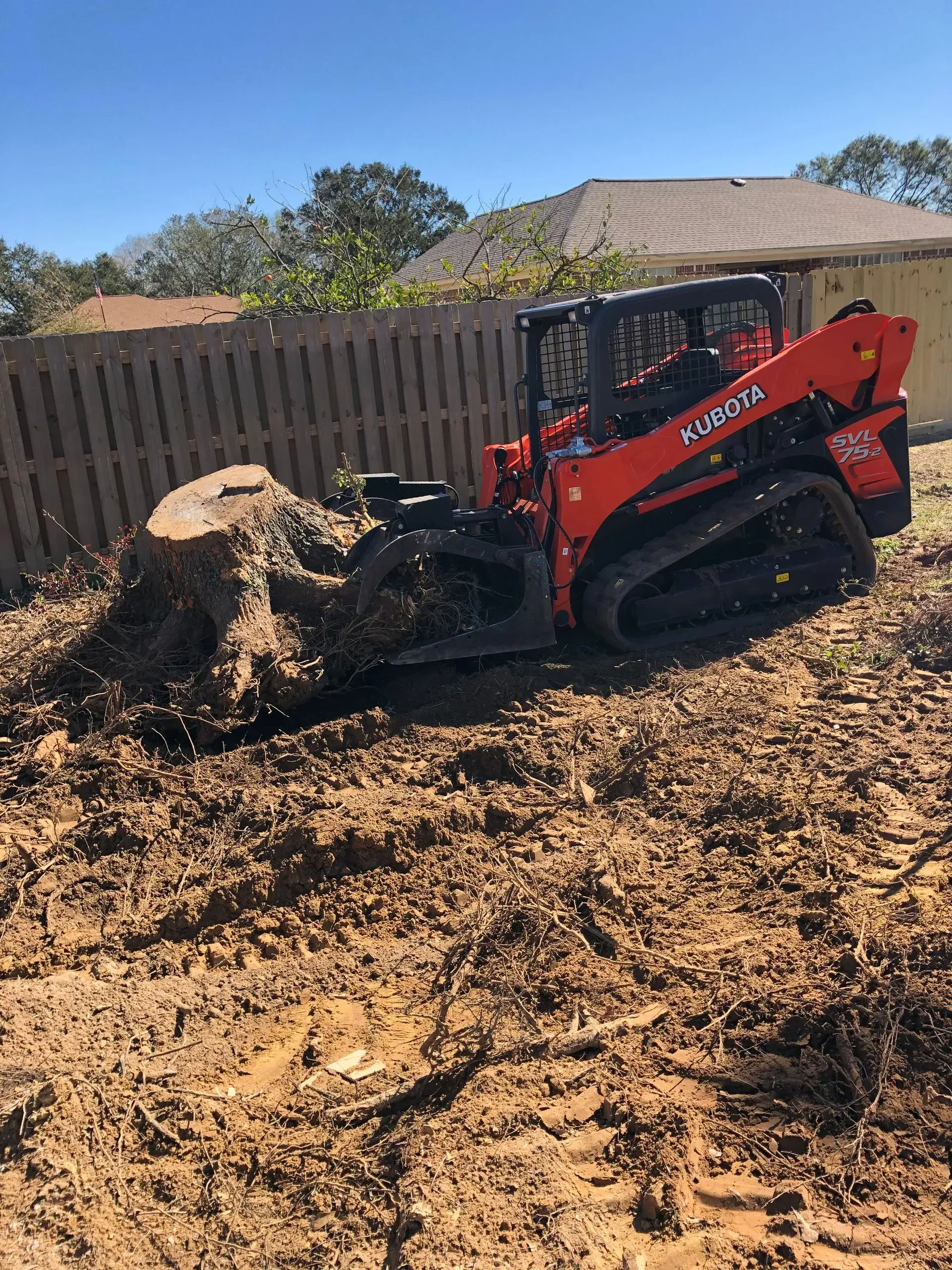 Orange Kubota track loader grinding a tree stump in a backyard.