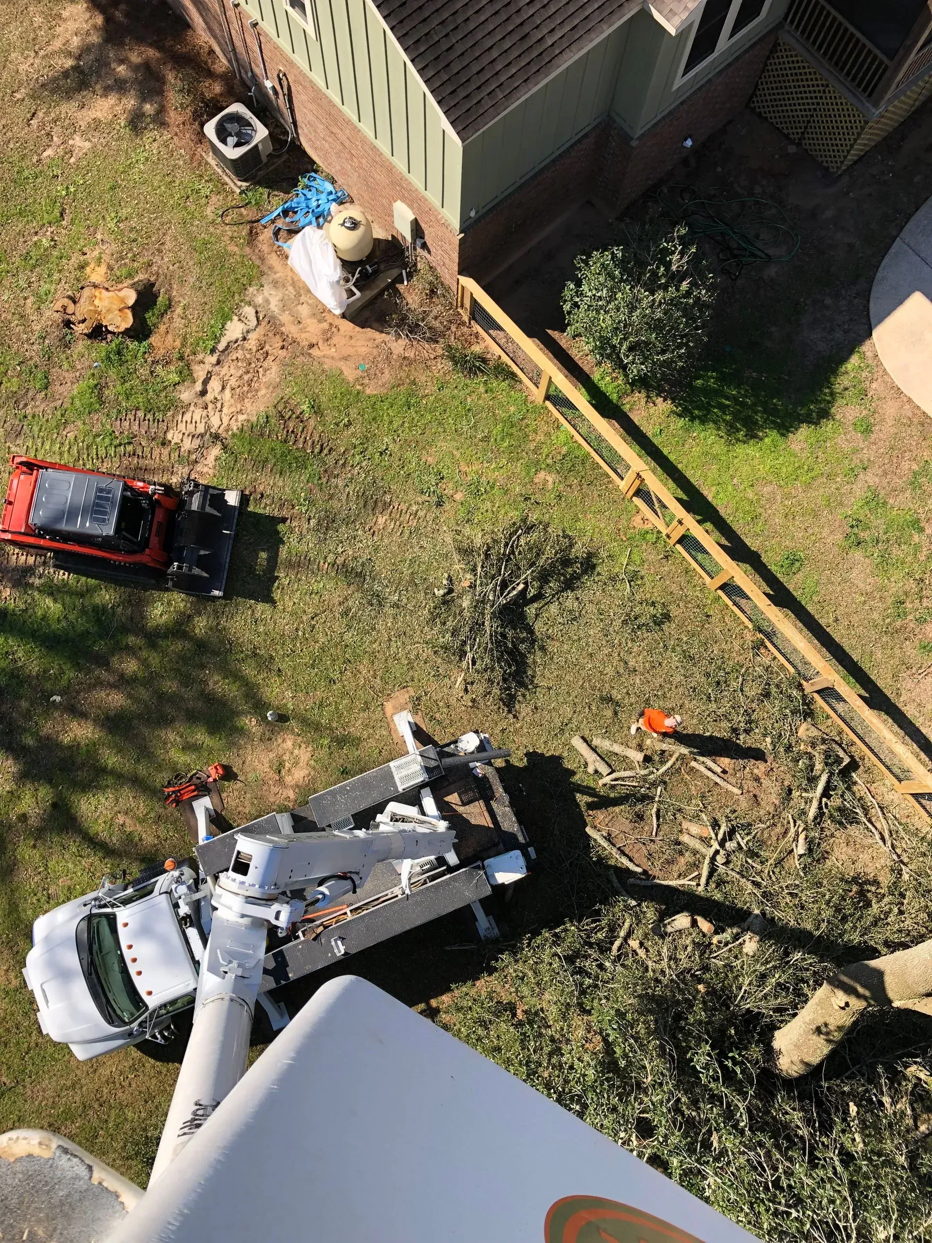 Overhead view of a white utility truck with a boom working near a house and fence.