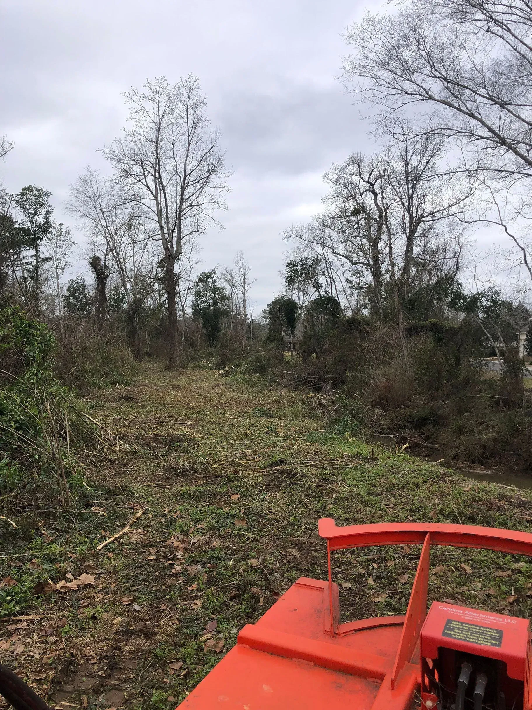 Field being cleared with an orange tractor; trees in background, cloudy sky.