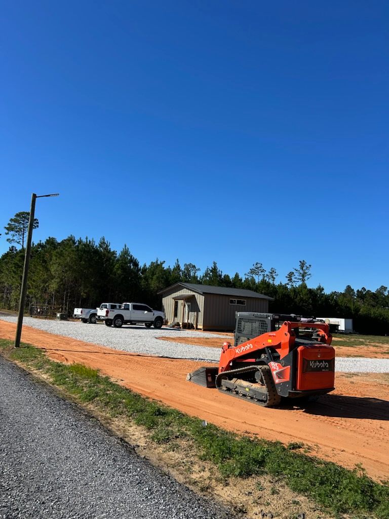 Orange skid steer on a dirt road, gravel driveway, gray shed, white truck, blue sky.