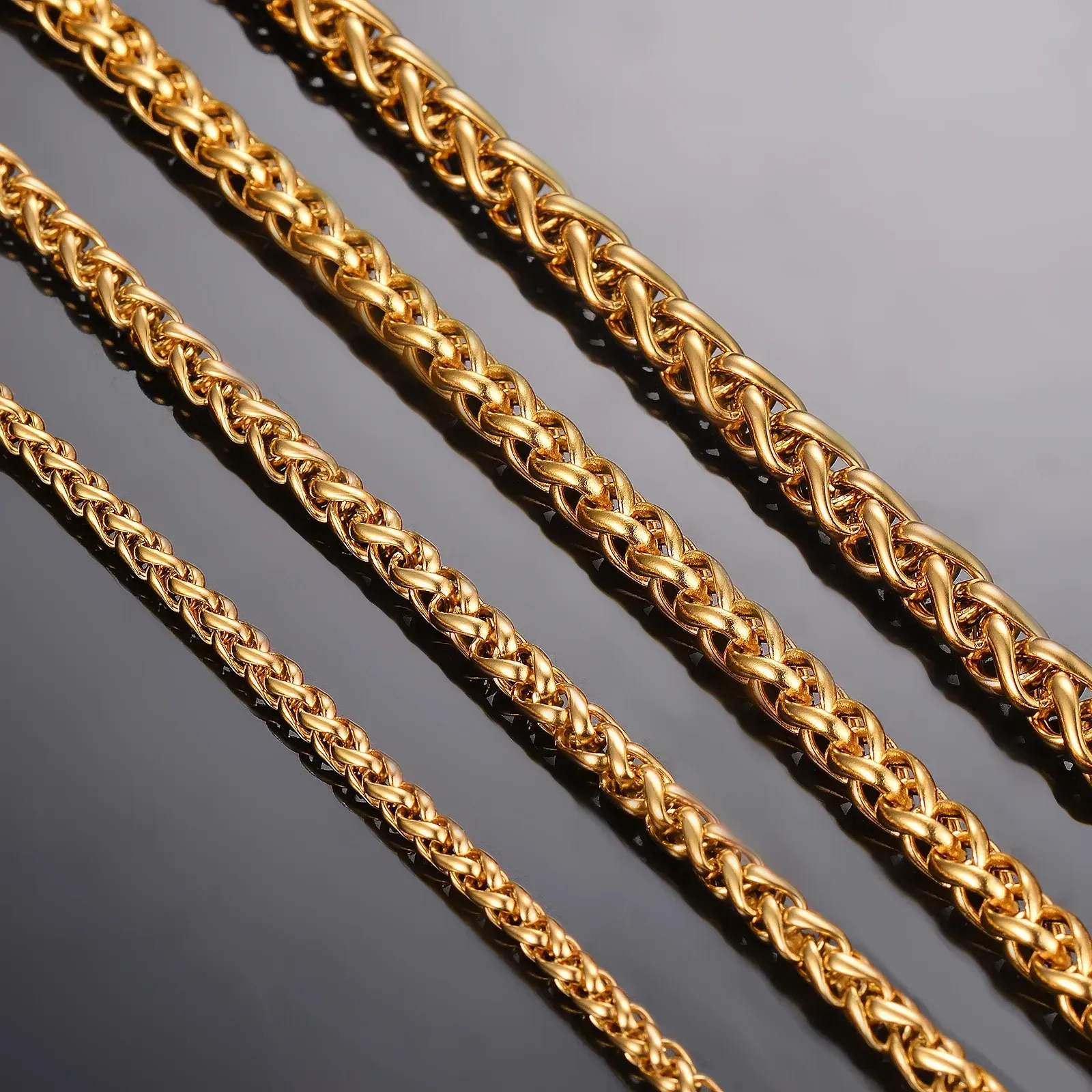 Gold wheat chain necklaces of varying thicknesses on a dark surface.