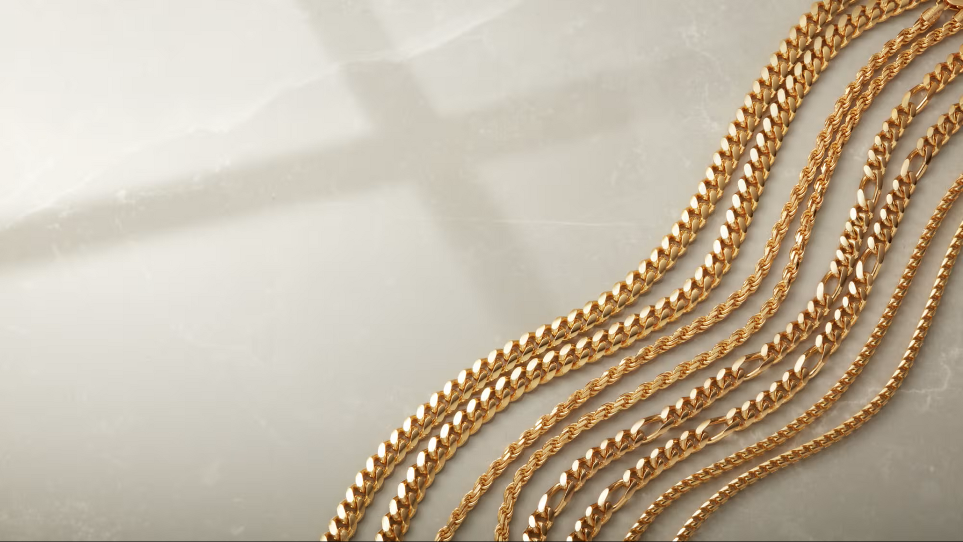 Gold chain necklaces arranged on a light-colored surface with a cross-shaped shadow.