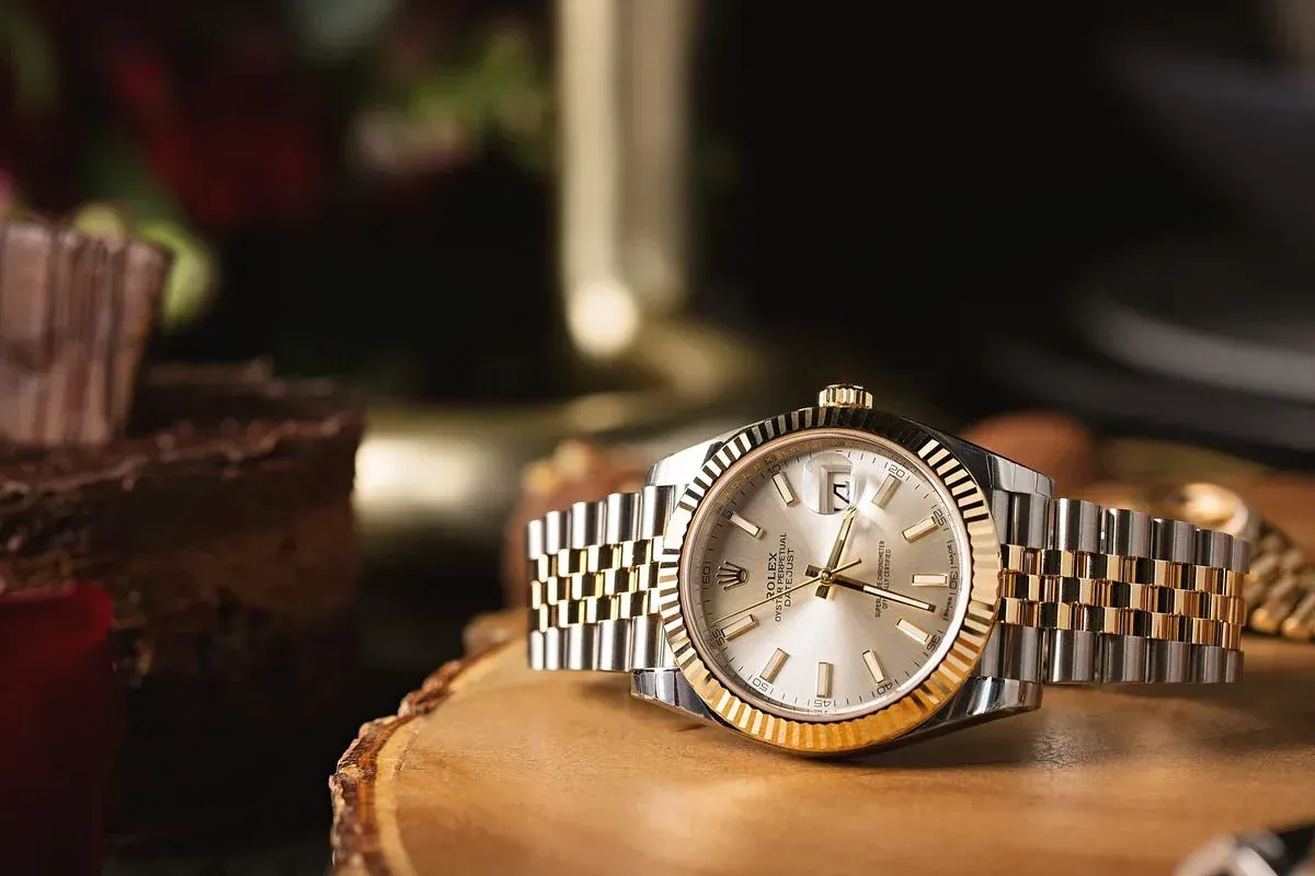 Rolex watch with gold and silver band, on a wood surface.