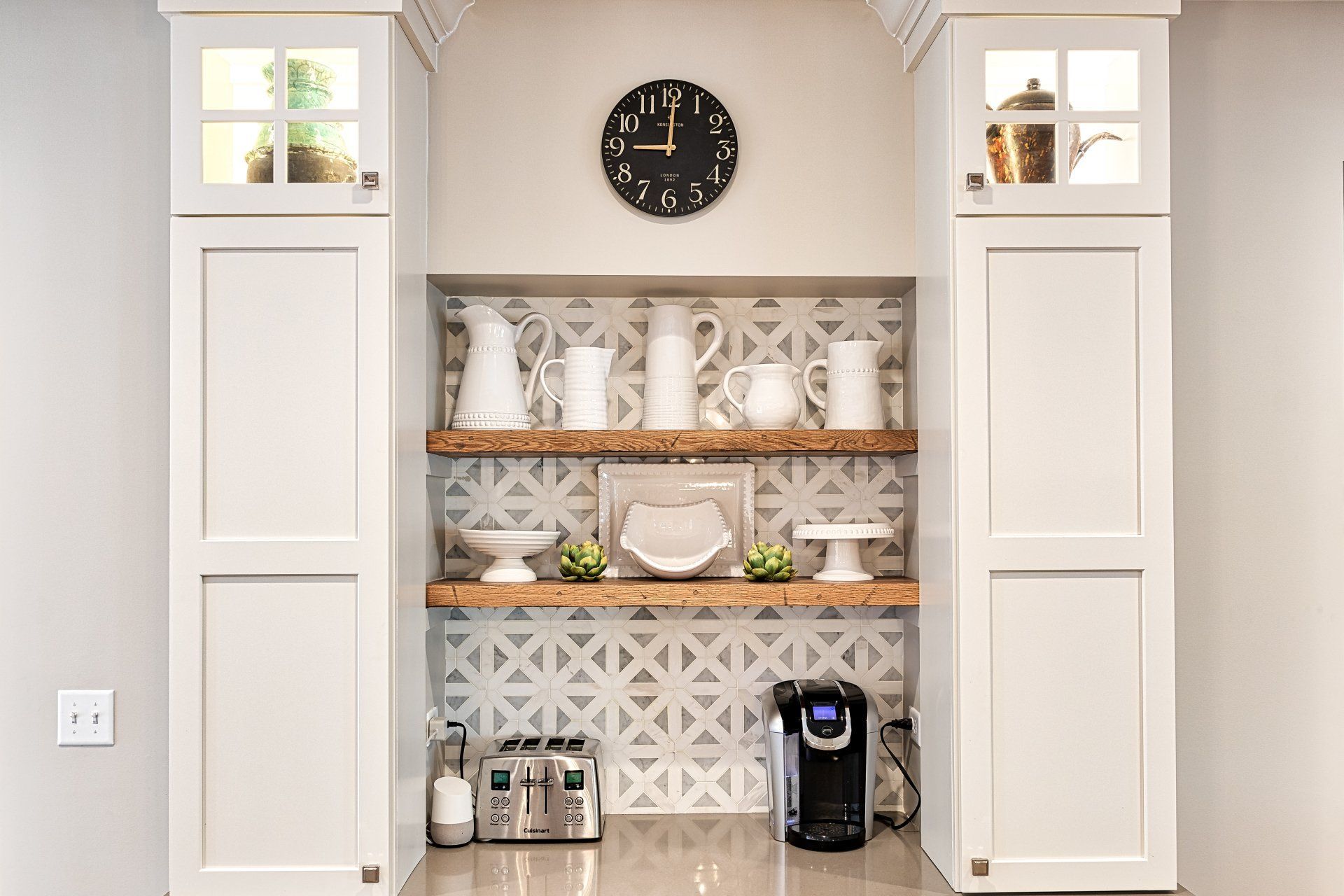 A kitchen with white cabinets , wooden shelves and a clock on the wall.