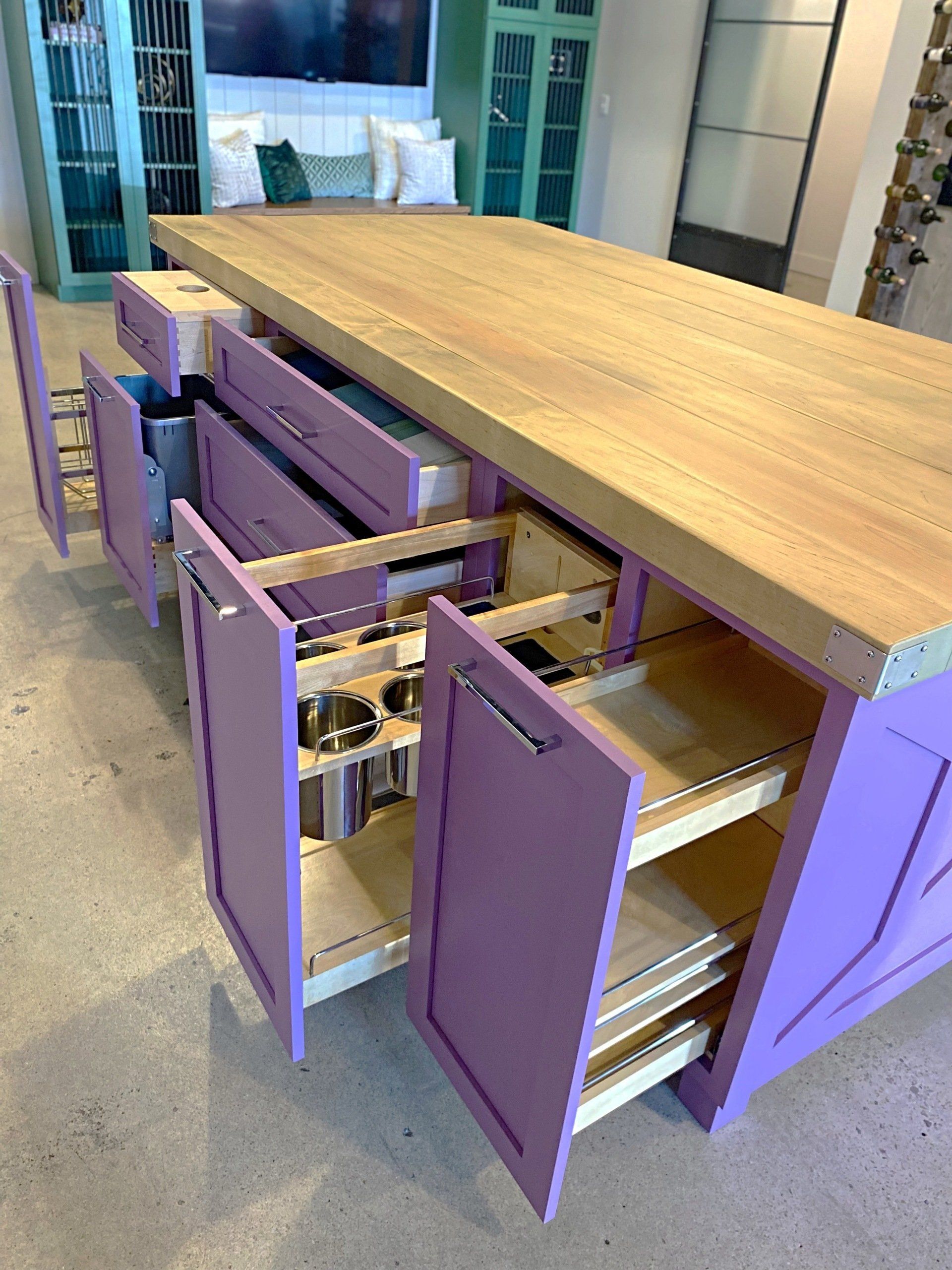 A kitchen island with purple cabinets and drawers and a wooden counter top.