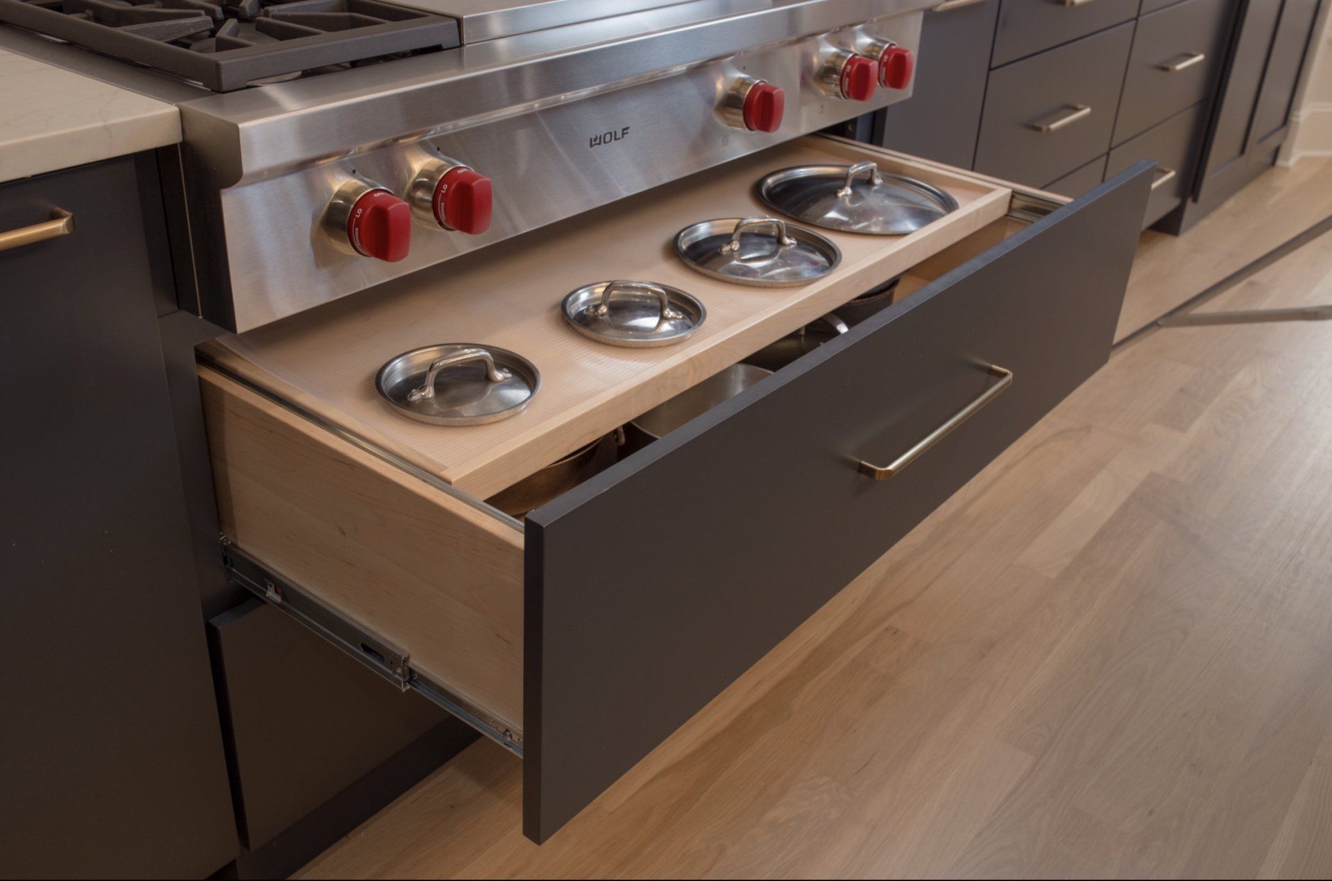 A kitchen with a stove top oven and a drawer filled with pots and pans.