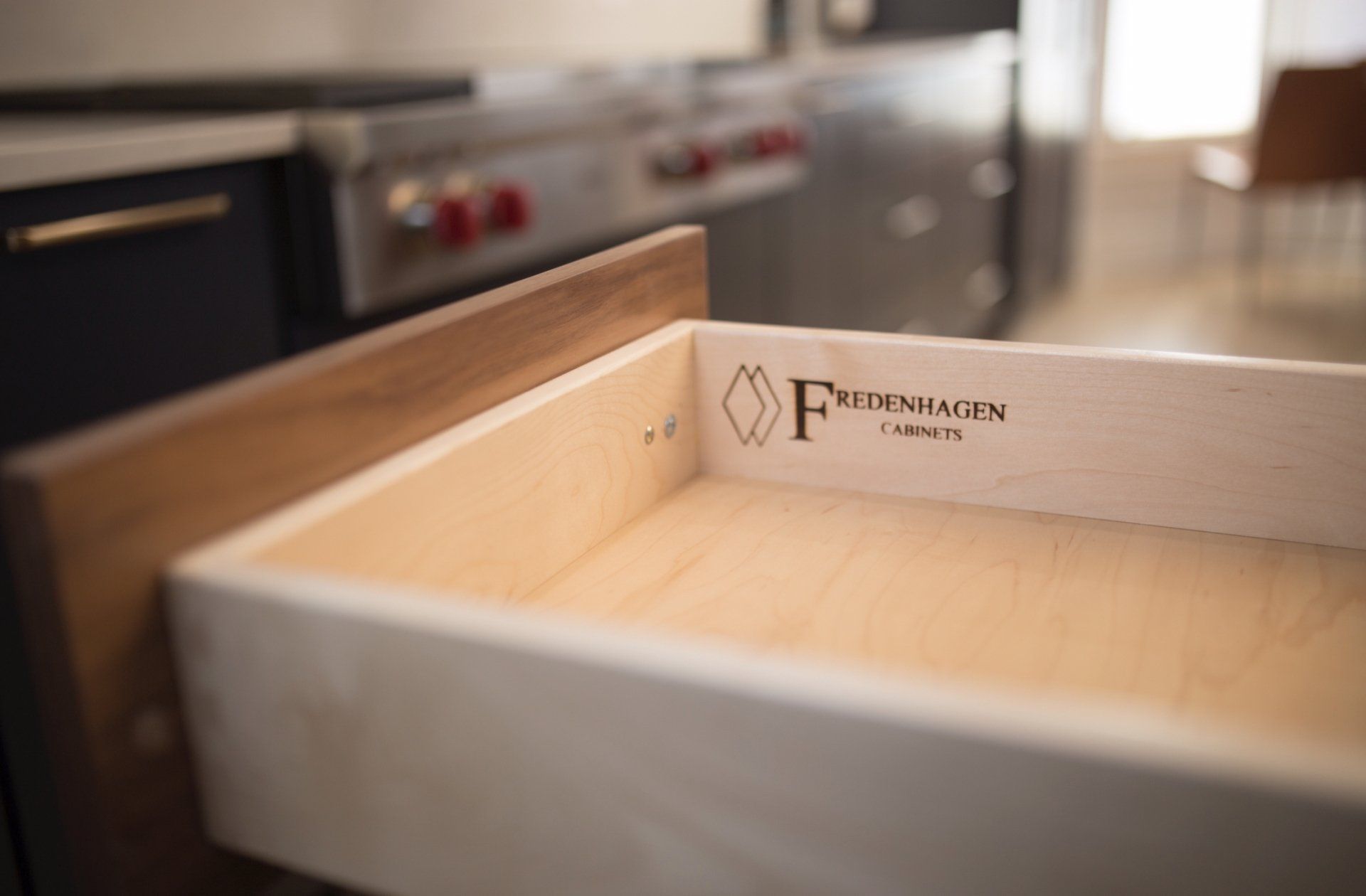 A wooden drawer is open in a kitchen with a stove in the background.