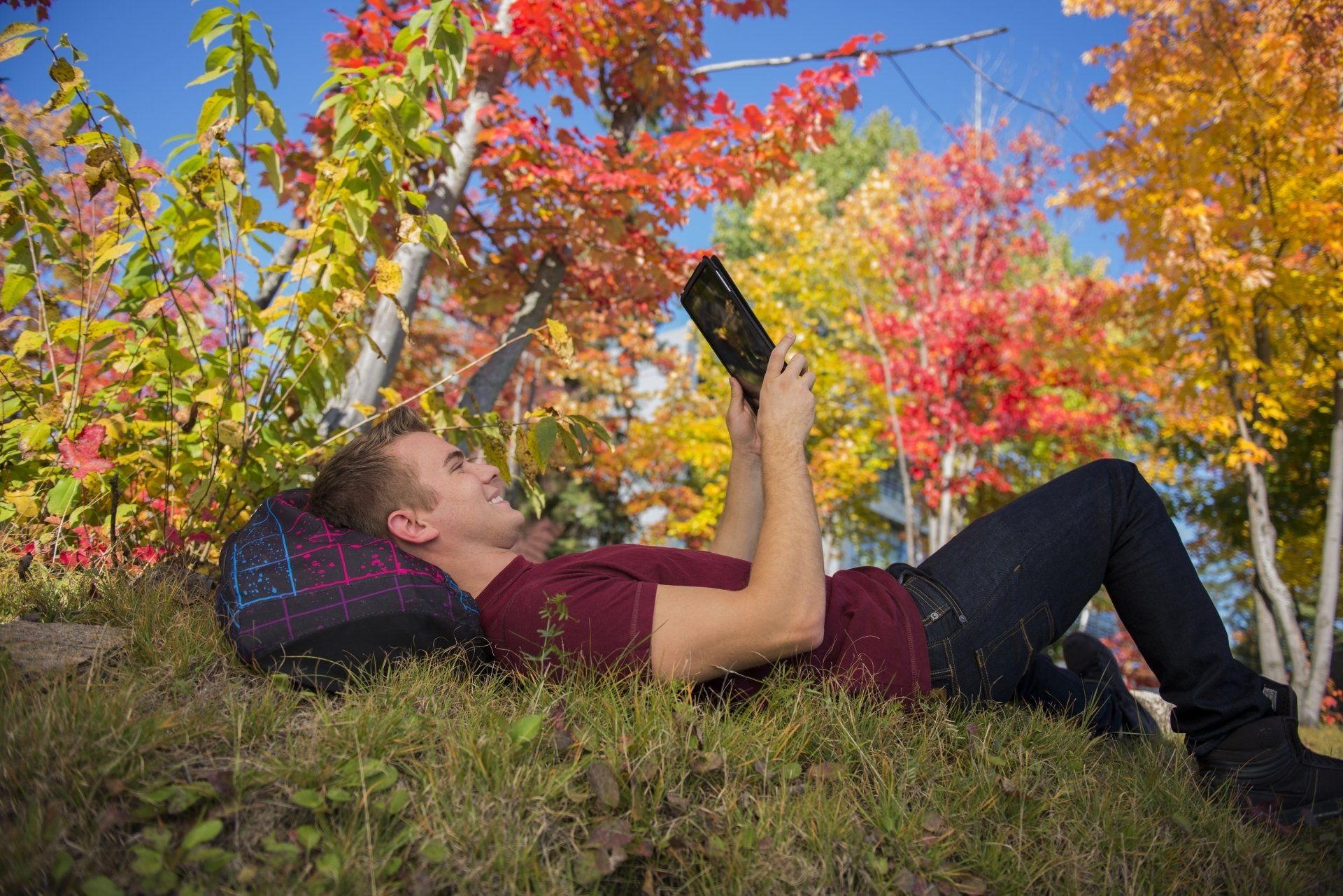 A man is laying on a hill reading a book.