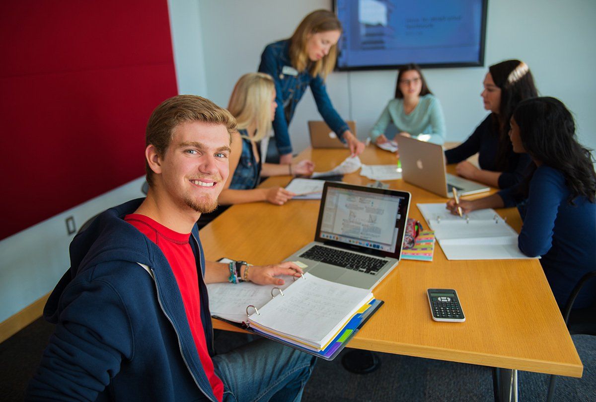 A group of people are sitting around a table with laptops and notebooks.