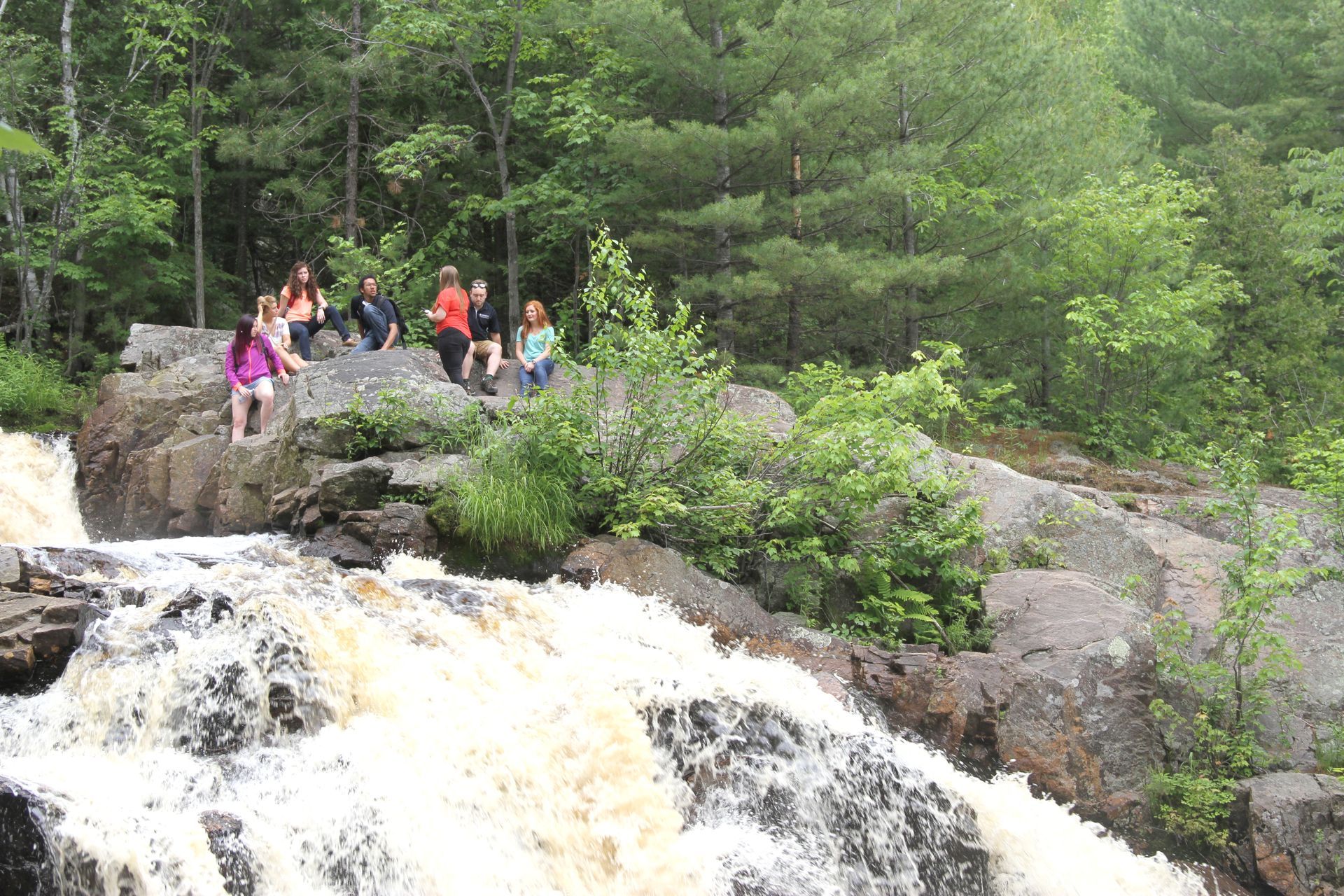 A group of people are sitting on a rock overlooking a waterfall.