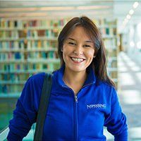 A woman in a blue jacket is smiling in a library.