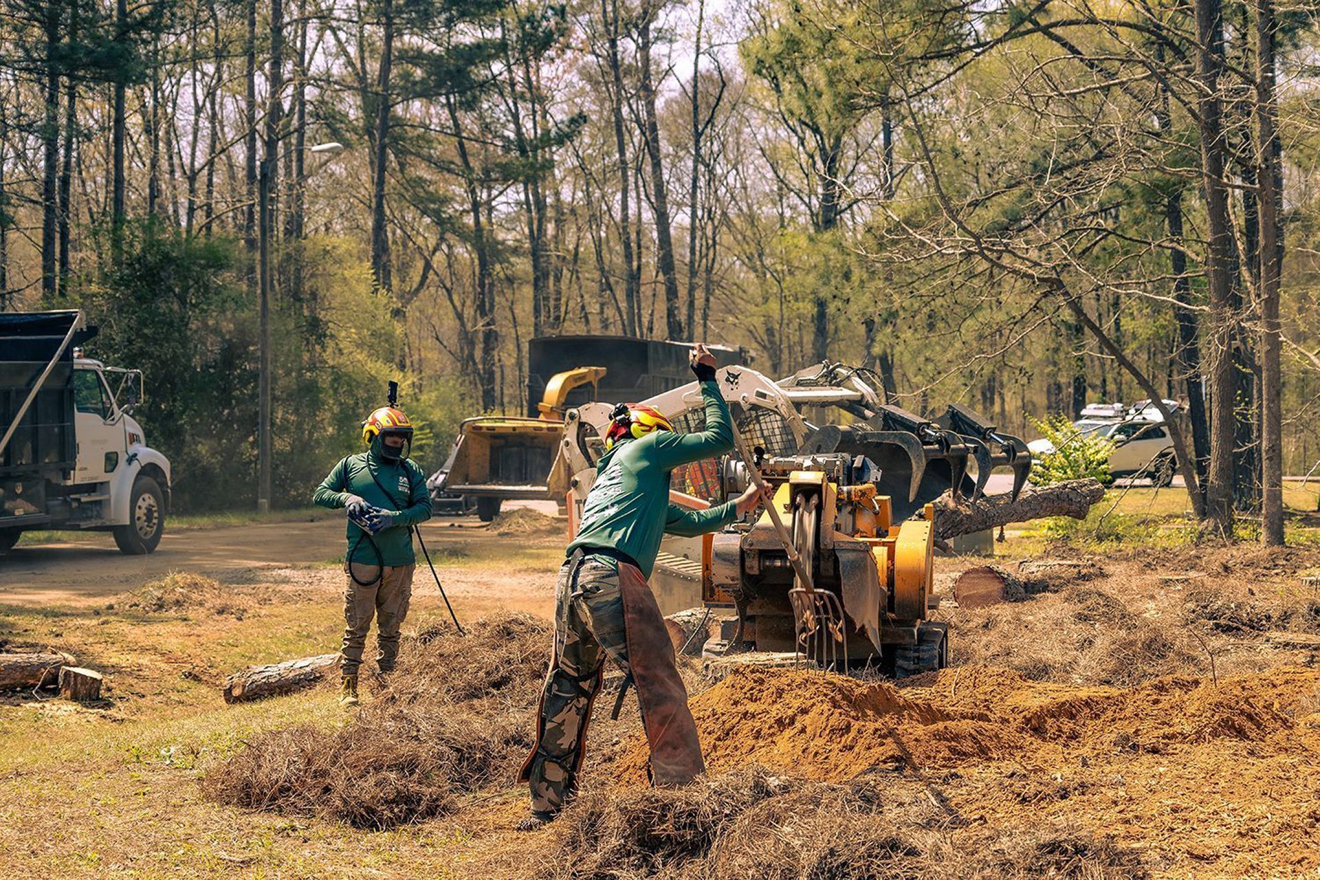 Two men are working on a stump grinder in the woods.