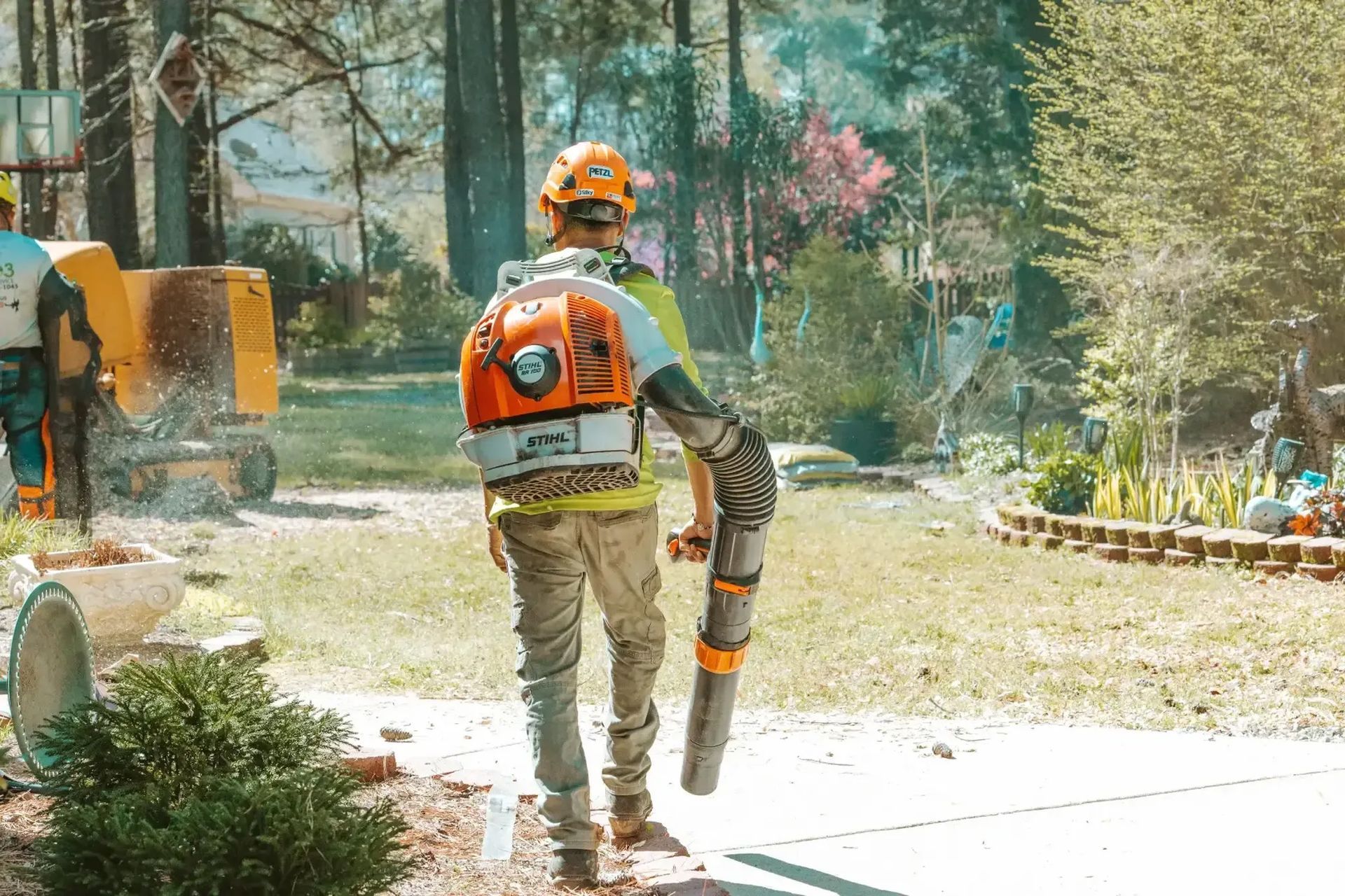 A man is walking down a sidewalk with a backpack blower.