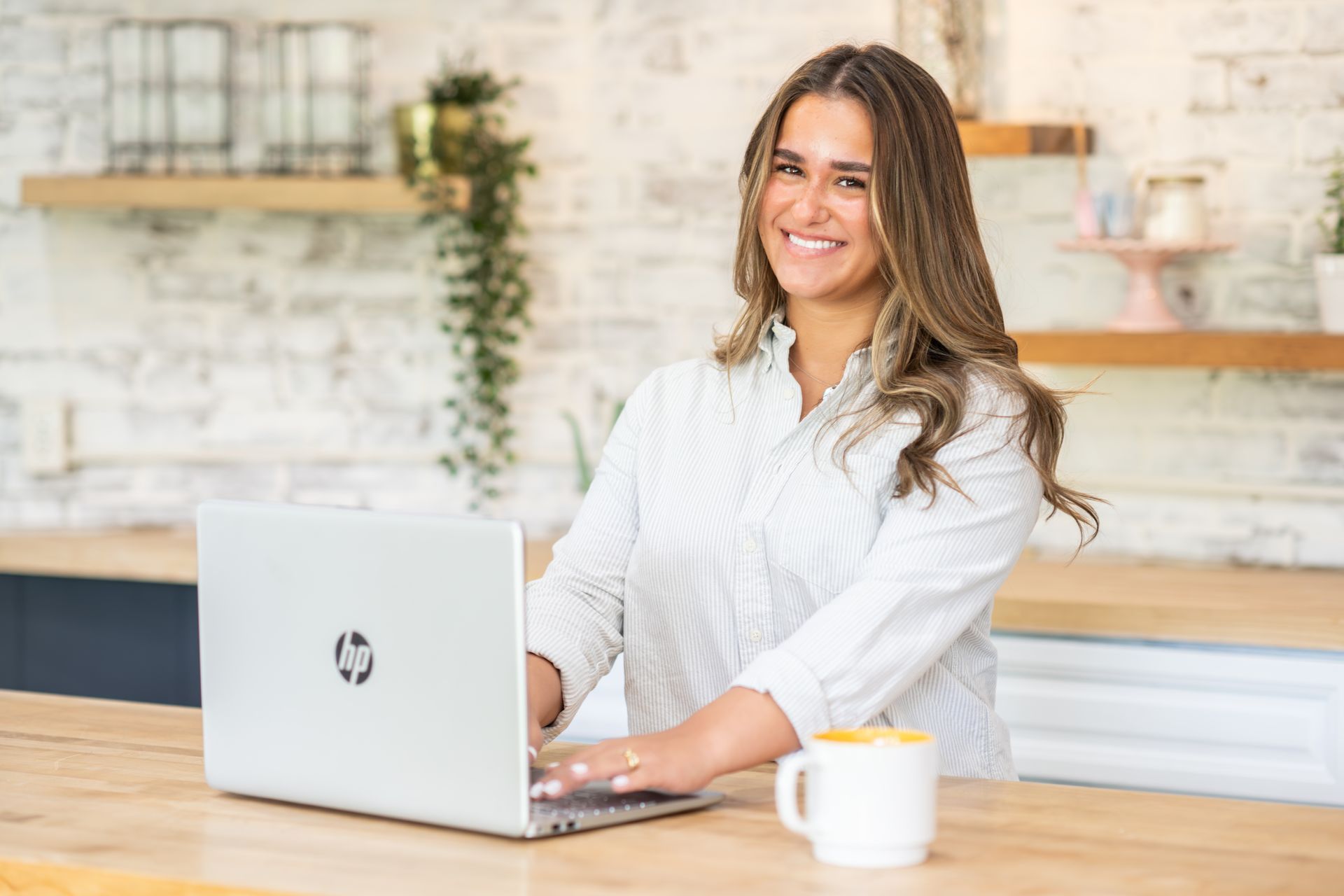 Woman small business owner smiles while working on a laptop at a kitchen counter. 