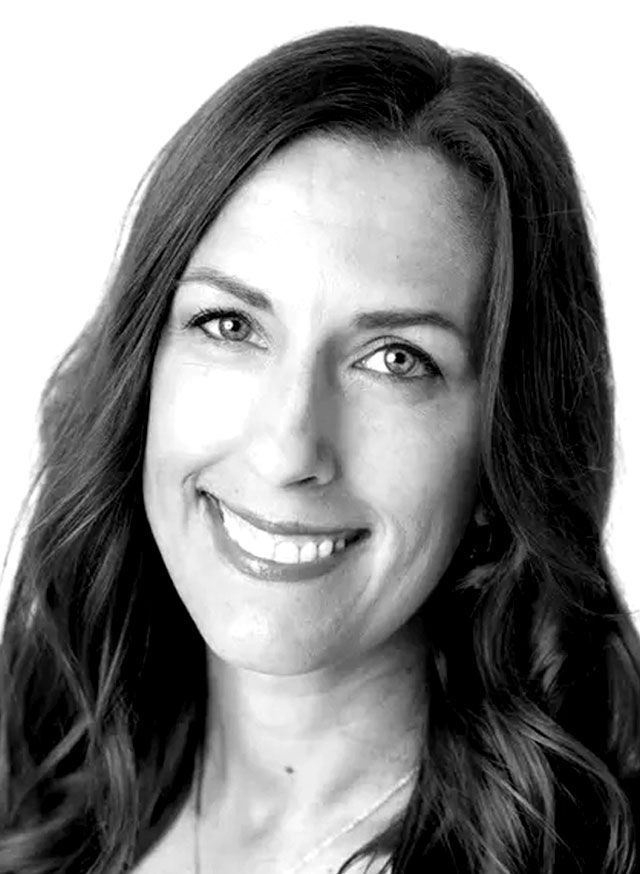 Woman with long, wavy hair smiles, looking towards the viewer in a close-up shot against a white background.