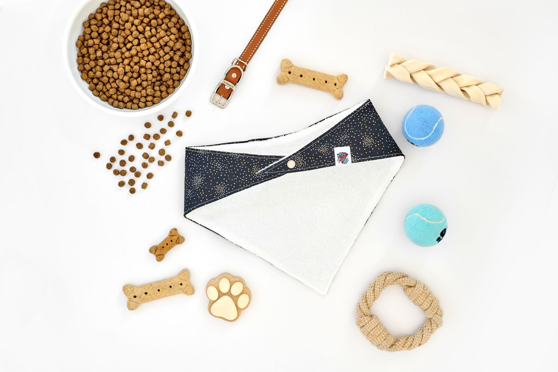 Dog bandana and accessories on a white surface: food bowl, treats, collar, balls, rope toy.