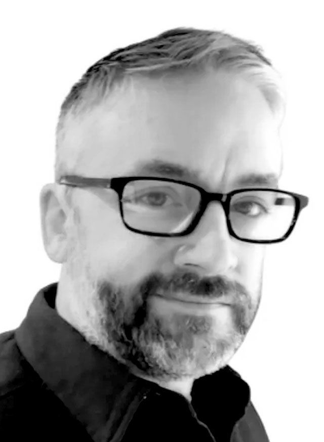 Man with glasses and beard, smiling, looking at the camera. Black and white, head and shoulders.