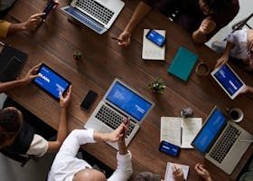 People at a wooden table with laptops, tablets, and phones, possibly a collaborative meeting.