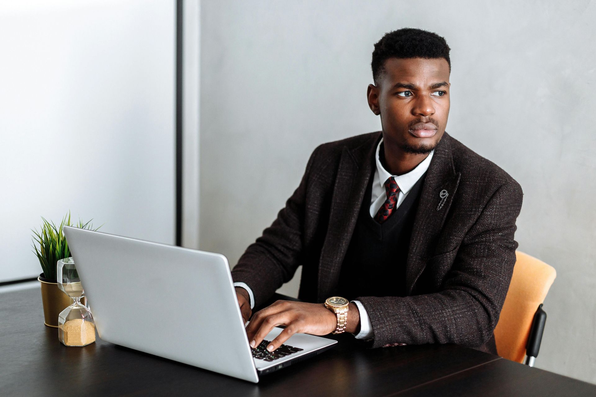 Man in suit using a laptop, looking off to the side, at a desk.