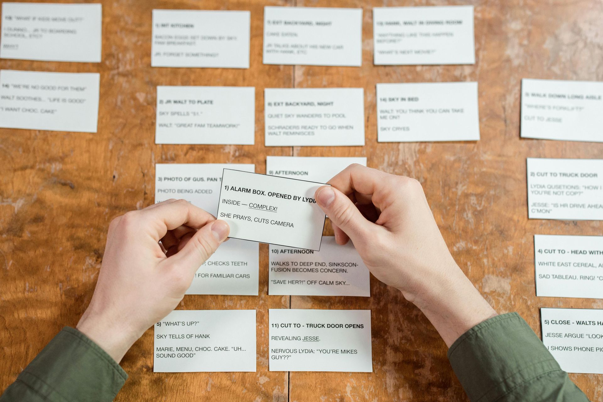 Hands holding a card above other cards pinned to a wooden surface, brainstorming process.