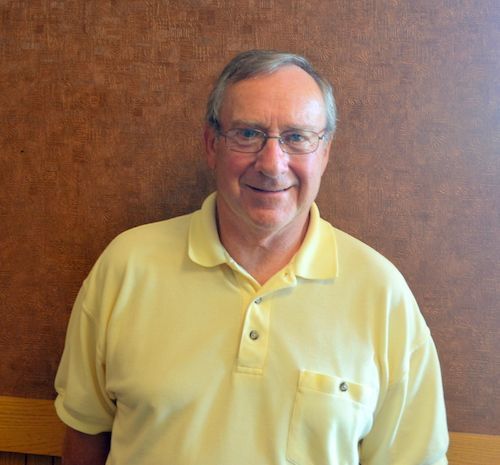 A man wearing glasses and a yellow shirt is smiling for the camera