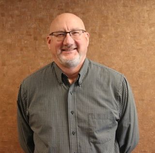 A bald man with glasses and a beard is smiling for the camera.