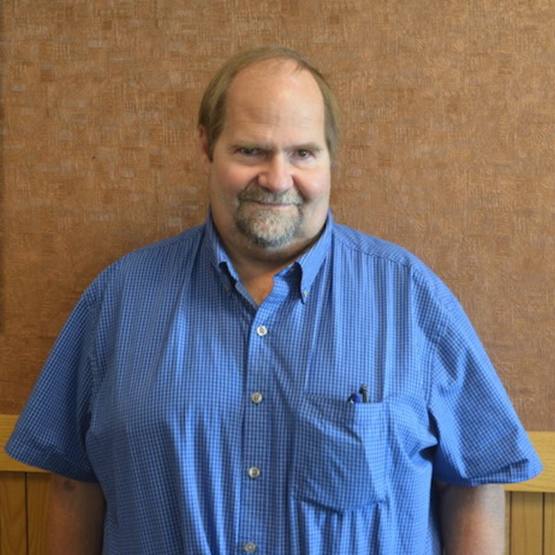 A man wearing glasses and a yellow shirt is smiling for the camera