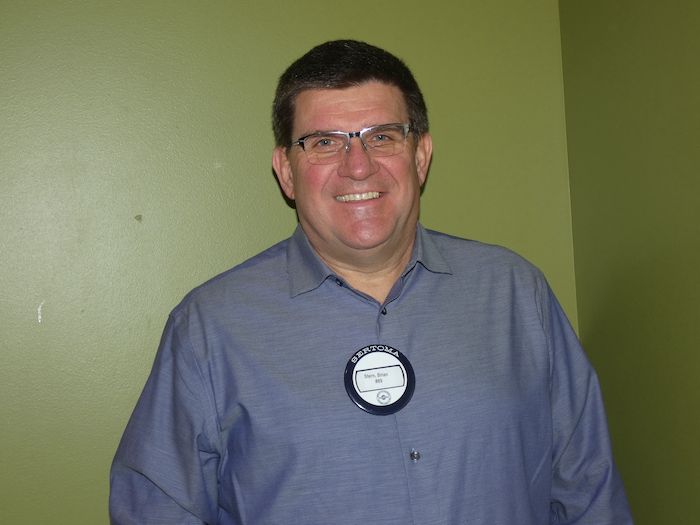 A man wearing glasses and a yellow shirt is smiling for the camera