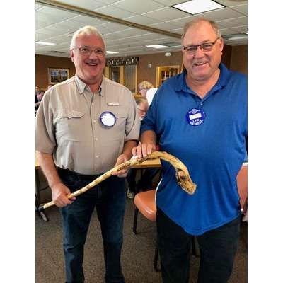 Two men are standing next to each other holding a cane.