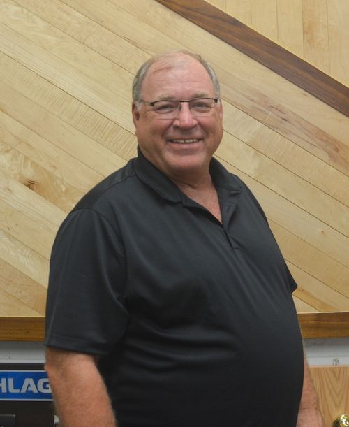 A man wearing glasses and a yellow shirt is smiling for the camera