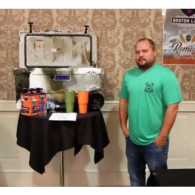 A man in a green shirt is standing in front of a table with a cooler on it.