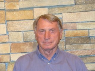 A man wearing glasses and a yellow shirt is smiling for the camera