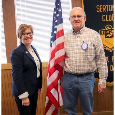 A man and a woman are standing next to an american flag.