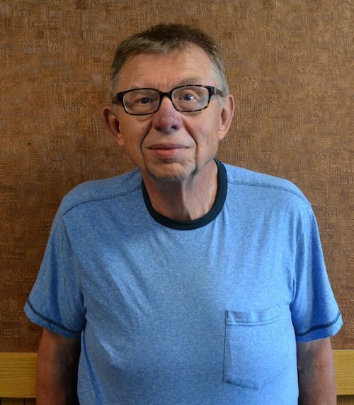 A man wearing glasses and a yellow shirt is smiling for the camera