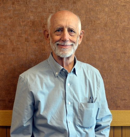 A bald man with glasses and a beard is smiling for the camera.