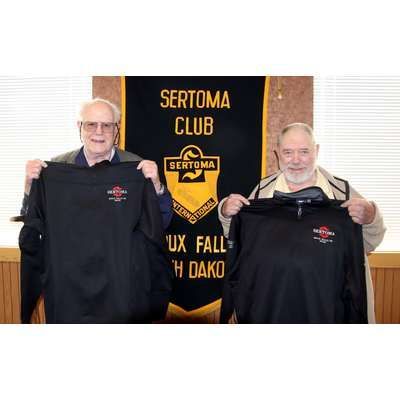Two men are holding shirts in front of a banner that says sertoma club