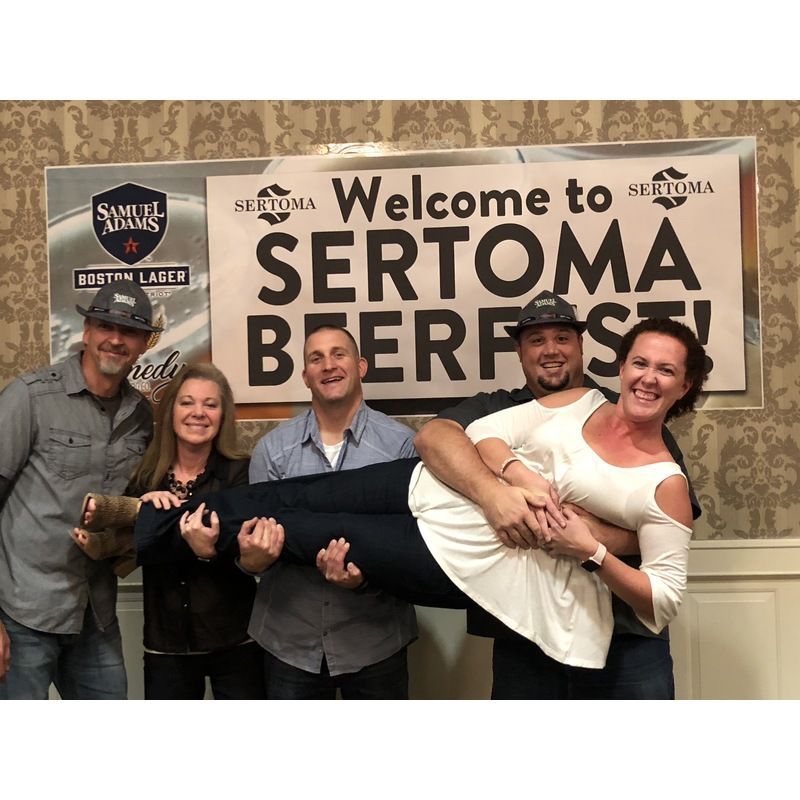 A group of people are posing for a picture in front of a sign that says welcome to sertoma beerfest.