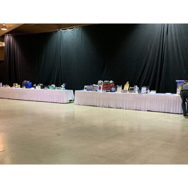 A row of long white tables in a room with a black curtain behind them.