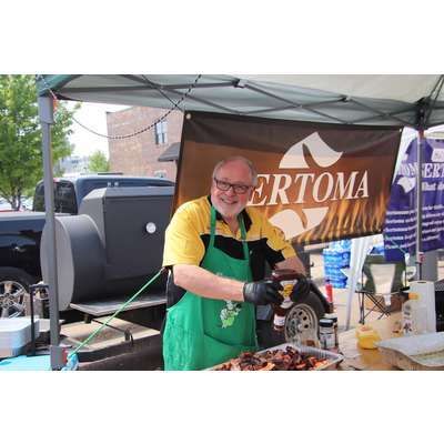 A man in a green apron is cooking food under a tent.