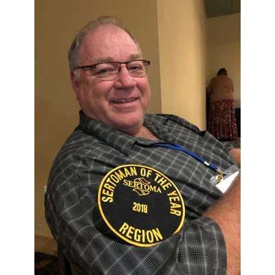 A man wearing glasses and a sertoman of the year patch on his arm.