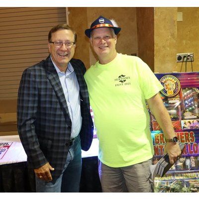 Two men are posing for a picture in front of a fireworks display