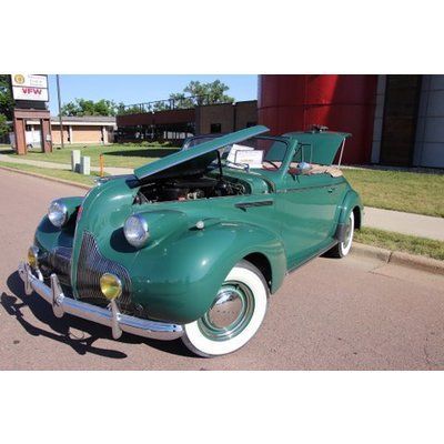 An old green car with the hood up is parked on the side of the road.