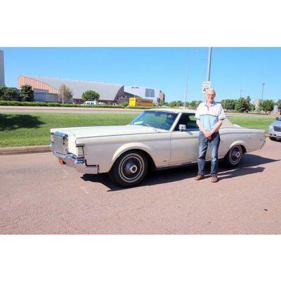 A man is standing next to a white car in a parking lot.