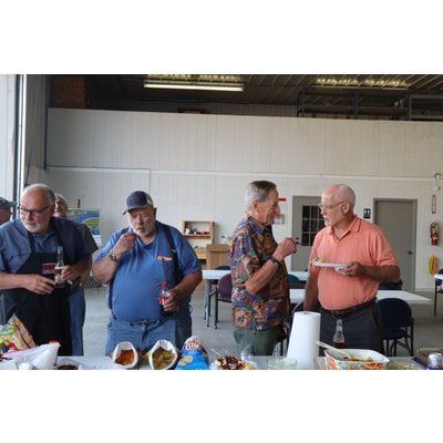 A group of men are standing around a table eating food.