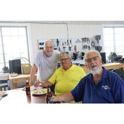 Three men are sitting at a table with bottles of beer and a plate of food.